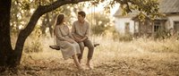 Young couple sitting on tree swing in golden sunlight sharing intimate moment in countryside setting for romantic lifestyle content.