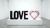 Bold black LOVE letters and red geometric heart sculpture displayed on a white pedestal in a modern gallery interior.