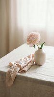 Single pink peony in cream ceramic vase on linen table with draped fabric, soft natural light, minimalist home decor styling.