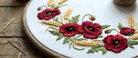 Red poppy flowers embroidered on white fabric in wooden hoop with needles on rustic table for handcraft and needlework projects.