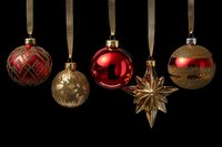 Elegant Christmas ornaments in red and gold hanging on ribbons against black background, festive holiday decorations for tree.