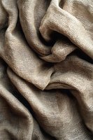 Natural linen fabric with soft folds and wrinkles creating abstract wavy pattern. Textured burlap material in neutral beige tones showing detailed weave structure.