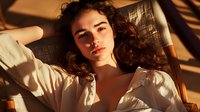 Young Mediterranean woman with dark curly hair lying in warm sunlight, wearing white blouse. Natural beauty portrait with dramatic shadows and golden hour lighting.