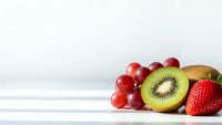 Fresh mixed fruits including red grapes, sliced kiwi and strawberry arranged on white wooden surface with copy space for healthy eating concepts.