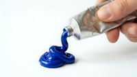 Hand squeezing blue acrylic paint from metal tube onto white surface for artistic projects and creative work.