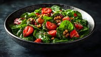 Fresh spinach salad with sliced strawberries and candied walnuts served in dark ceramic bowl on moody black background. Healthy vegetarian meal.