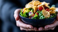 Fresh mixed greens salad with cranberries and nuts in dark bowl held by hands, healthy eating concept for restaurant menus and dietary lifestyle content.