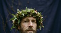 Middle-aged Caucasian man wearing natural green foliage crown headpiece with ferns and leaves against dark blue background for creative portrait photography.