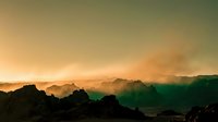 Silhouetted mountain peaks against golden sunrise sky with emerald green valley mist below, creating dramatic landscape scenery for nature and travel projects.