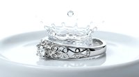 Elegant diamond engagement ring with ornate band creating water splash crown effect on white surface for luxury jewelry advertising and wedding concepts.