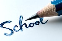 Handwritten word "School" in blue ink with graphite pencil tip above, shown in macro photography on white paper. Educational concept for learning and literacy.