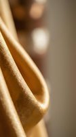 Closeup of golden satin fabric with soft folds and luxurious sheen, suitable for fashion, textile, and luxury product design backgrounds.