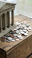Miniature bank building with classical columns surrounded by scattered coins on wooden surface representing financial institutions and money management.