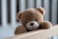 Cute brown teddy bear with smiling face peeking over wooden shelf edge, soft plush toy against blurred background creates cozy nursery atmosphere.