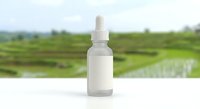 Frosted glass dropper bottle with white cap on clean surface against blurred green agricultural field background for natural skincare and wellness products.