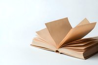 Open book with blank cream pages fanning out against white background, creating soft shadows and minimalist composition for reading, education, and literature concepts.
