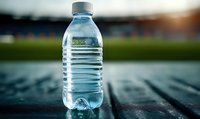 Clear plastic water bottle on wooden surface with blurred sports field in background, golden sunset light creating refreshing hydration scene.