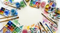 Overhead view of colorful watercolor paints, brushes, and art supplies arranged in a circle on white background with empty center space for creative projects and artistic design work.