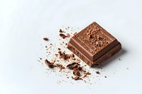 Broken piece of milk chocolate bar with scattered crumbs and cocoa powder on white background, minimalist food photography composition for confectionery advertising.