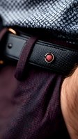 Luxury leather belt with red metallic button detail on textured fabric background, showcasing premium fashion accessories and elegant menswear details.