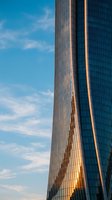 Modern skyscraper with reflective glass facade and vertical ribbed metal columns catching golden sunlight against clear blue sky, suitable for corporate and architectural projects.