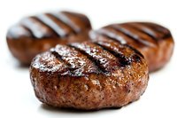Juicy grilled beef patties with classic char marks and seasoning on white background, close-up view showing texture and caramelization for food marketing.