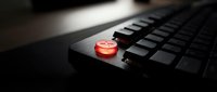 Red emergency stop button on black keyboard for safety protocols and system shutdown procedures in industrial computing environments.