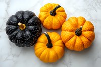 Fresh orange mini pumpkins and black decorative gourd arranged on white marble background, seasonal autumn harvest produce for Halloween and fall decor.