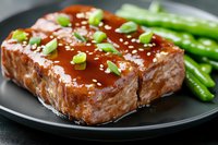 Glazed salmon fillet with teriyaki sauce, sesame seeds and chopped green onions served with steamed green beans on black plate, close up view.