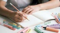 Young woman artist drawing in sketchbook with colorful markers and pencils on white desk. Creative hobby, art education, design process concept.