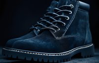 Navy blue suede boot with white contrast stitching and rugged sole on dark background. Close-up view shows detailed lacing system and craftsmanship details.