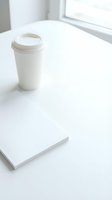 White takeaway coffee cup with lid on minimalist workspace table next to blank notepad, bright window light, mockup for branding and design projects.