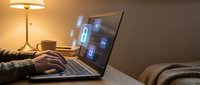 Person using laptop with digital security icons on screen in cozy evening home office setting with warm lighting and coffee cup on desk.