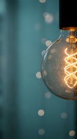 Vintage Edison bulb with warm glowing filament against teal background with soft bokeh lights for modern interior design and lighting concepts.