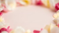 Soft pink background with scattered rose petals and golden bokeh lights creating romantic atmosphere for wedding invitations and Valentine's Day designs.
