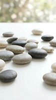 Smooth river stones and pebbles in neutral tones arranged on white surface with blurred natural background, suitable for wellness, spa, meditation and zen design projects.