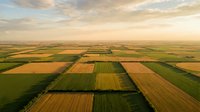 Aerial view of patchwork agricultural fields creating geometric patterns across rural farmland during golden hour sunset with dramatic sky.