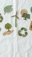 Paper cut eco icons on white fabric: recycling symbol, wind turbine, solar panel, green leaf, tree in hand, for sustainability design.