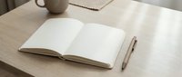 Open blank notebook with pen on wooden desk workspace for writing planning and creative projects in minimalist home office setting.