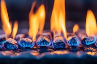 Bright orange flames dance atop blue gas burner elements in macro view, creating dramatic contrast between warm and cool tones in dark ambient setting.