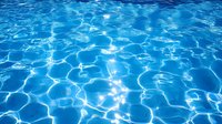 Rippling blue water surface with sunlight creating bright caustic patterns and reflections, showing clear swimming pool water on sunny summer day.