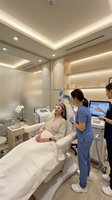 Professional skincare treatment session in modern medical spa with Asian female patient receiving facial therapy from skilled aesthetician using advanced equipment.