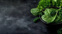 Fresh green spinach leaves and curly kale in black ceramic bowl on dark moody background with water drops and copy space for healthy eating concept.