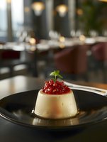 Creamy vanilla panna cotta topped with vibrant red berry compote and fresh mint leaf served on black ceramic plate in upscale restaurant setting.