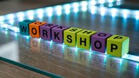 Colorful alphabet blocks spelling WORKSHOP on glass surface with LED lighting creating modern educational training concept for business development.