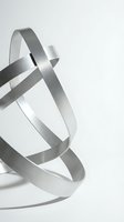 Abstract metallic ribbons flowing in elegant curves creating dynamic sculptural forms on white background for modern design projects.