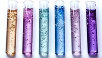 Colorful test tubes with bubbling liquids in gold, pink, teal, blue, lavender, and purple shades arranged in row for scientific experiment or laboratory research.