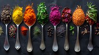 Vibrant colorful spices and herbs in vintage silver spoons on dark background, overhead view of aromatic seasonings arranged in creative food composition.