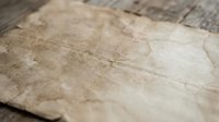 Aged parchment paper with weathered texture and brown stains on rustic wooden surface for vintage design projects and historical themed artwork.