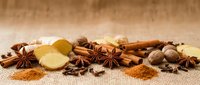 Cinnamon sticks, star anise, ginger root, and nutmeg arranged on burlap fabric for culinary and baking applications.